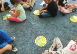 Dzieci na dywanie układają z części kolorowe kropki.